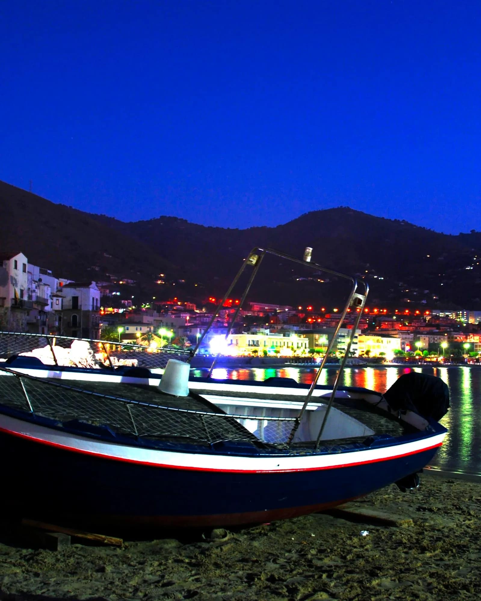 Il porto vecchio la sera: una barca sulla sabbia, le luci del paese sull'acqua