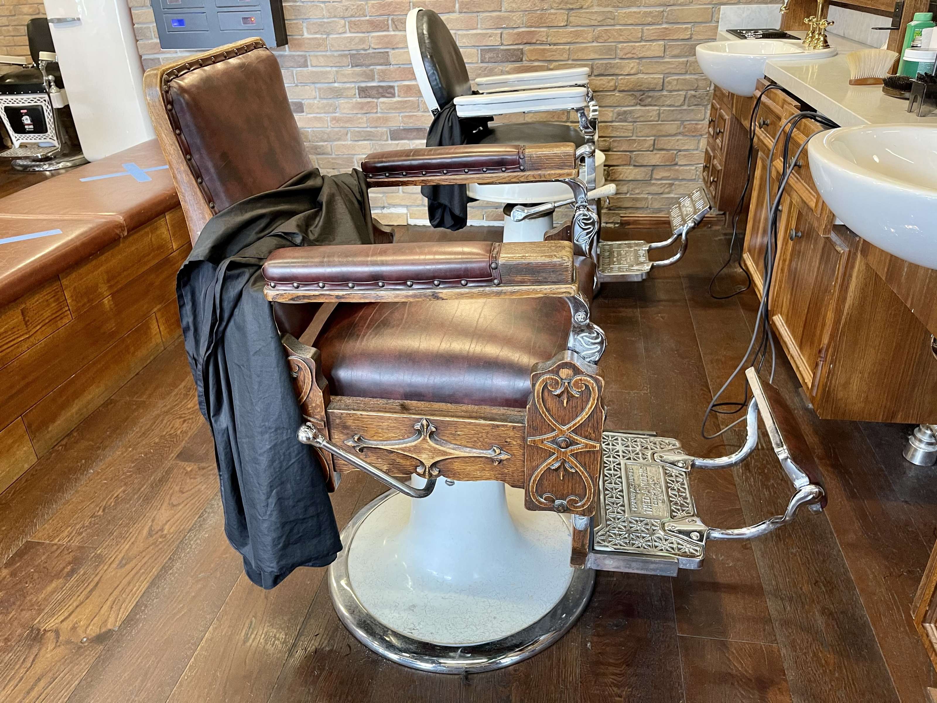 La sala di NOIR Barber Club: la poltrona in pelle con la mantella, il parquet, i lavabi in fila