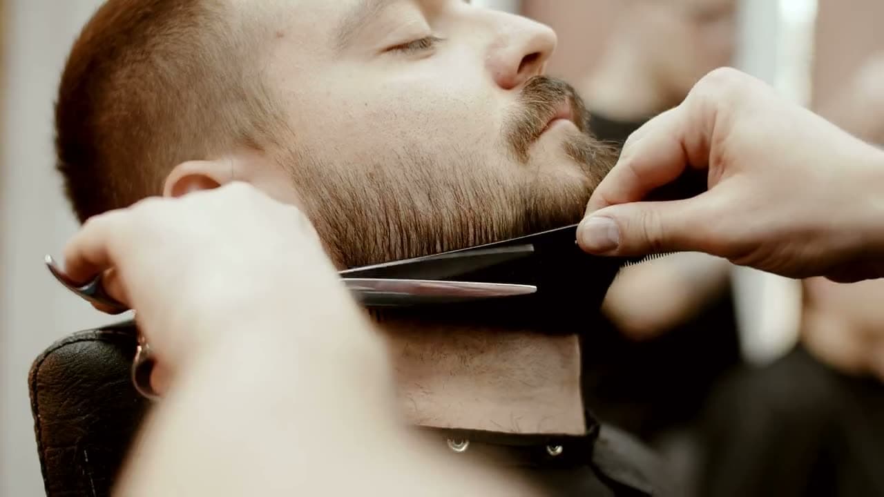 Le forbici e il pettine sulla barba, il cliente a occhi chiusi